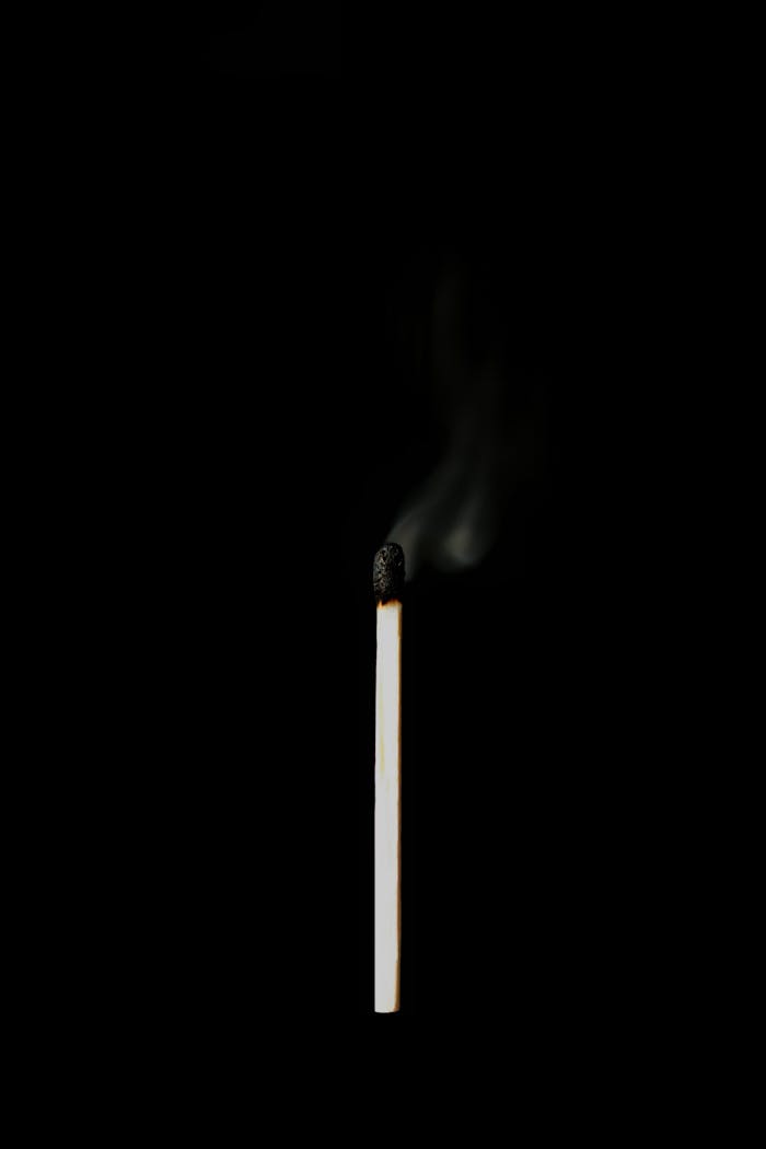 A single burnt matchstick with smoke rising against a dark background.